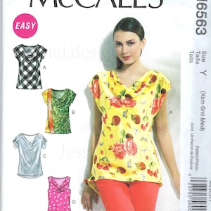 May include: McCall's sewing pattern M6563. The pattern includes designs for various tops, including a cowl neck top. The image shows a woman wearing a yellow top with a floral print and red pants. The word "EASY" is in a pink circle.