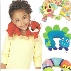 May include: Simplicity pattern 1518 featuring various stuffed animal neck pillows. The image shows a child wearing a red fox neck pillow. Other designs include a dog, a dinosaur, and a caterpillar. The pattern is one size.