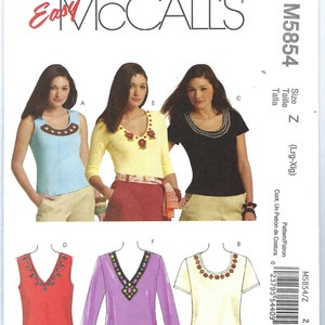 May include: McCall's sewing pattern M5854 featuring various tops. The pattern includes a sleeveless light blue top, a yellow long-sleeve top, and a black short-sleeve top, all with decorative necklines. Additional top designs are shown in red, purple, and cream.