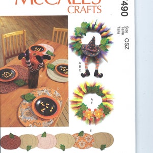 May include: McCall's Crafts pattern for Halloween decorations. The image shows a witch-themed wreath, pumpkin-shaped placemats, and a vase with witch legs. The pattern includes instructions for creating festive table settings and decorations.