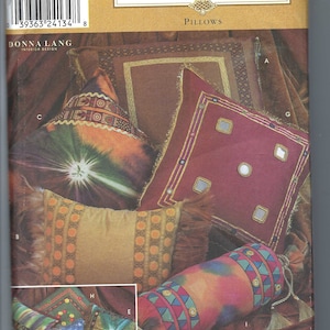 May include: A sewing pattern for home pillows with a variety of designs. The pattern includes a red pillow with gold trim and mirrored accents, a gold pillow with orange and brown trim, a brown pillow with gold trim, a cylindrical pillow with a colorful geometric pattern, and a green pillow with gold trim.