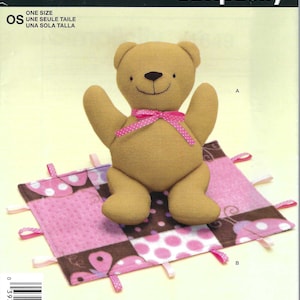 May include: A sewing pattern for a brown teddy bear with a pink bow and a pink and brown patchwork blanket. The pattern is from Simplicity and is for one size. The pattern number is 1649.