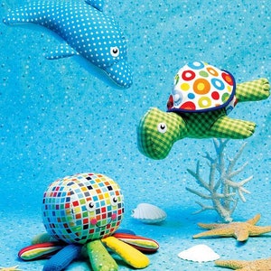 May include: A set of three plush ocean animal toys: a blue and white polka dot dolphin, a green and white checkered turtle with a colorful shell, and a colorful octopus with a mosaic-like pattern.
