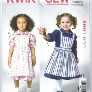 May include: Kwik Sew pattern K3962 for toddler dresses. The pattern features two different dress styles. One dress is pink with a floral print, and the other is blue and white striped with a solid blue trim. The pattern includes sizes T1-T4.