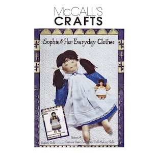 以下が含まれることがあります： ソフィーという名前のラグドール用のMcCall's Craftsパターン。人形は青い襟と袖が付いた白いドレスを着ています。パターンには、基本的な縫製と人形作りのスキルに関する指示が含まれています。