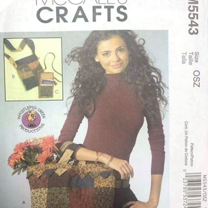 Könnte beinhalten: McCall's Crafts Schnittmuster M5543. Das Bild zeigt eine Frau mit langen, lockigen Haaren, die ein weinrotes Langarmshirt trägt und eine Patchwork-Tragetasche mit Blumen hält. Das Schnittmuster enthält Anleitungen für eine Tragetasche und zwei kleine Taschen.