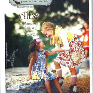 May include: Two girls wearing dresses are standing in a garden setting. The girl on the left is wearing a blue and white patterned dress with a yellow sash. The girl on the right is wearing a yellow and white dress with a red and white patterned skirt. The text on the image reads "Violette Field Threads patterns and tutorials Stylish threads you'll Alba Cowl neck dress with cargo pockets Sizes 2T-10 Years F751 USA $10.95 CAN $13.00".