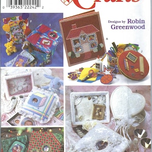 May include: A Simplicity Crafts pattern booklet with designs for making photo albums and boxes. The cover features a red heart with a white cross in the center and the words "Simplicity Crafts" in red letters. The booklet includes instructions for making a variety of photo albums and boxes, including a house-shaped album, a heart-shaped box, and a square box with a lace trim. The booklet also includes instructions for making a variety of embellishments, such as flowers, ribbons, and buttons.