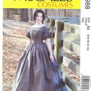 May include: A McCall's Costumes sewing pattern for a dress, size A5 (6-8-10-12-14). The pattern features a woman wearing a long, plaid dress with a fitted bodice and a full skirt. The dress has a gathered neckline and a small, ruffled collar. The woman is standing in front of a wooden fence.
