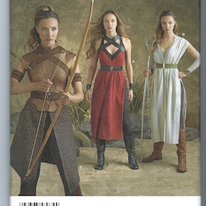 Peut inclure: Le patron de couture Simplicity 8074 présente trois modèles de costumes. La couverture montre des femmes dans des tenues sur le thème de la fantaisie, dont une robe rouge avec des accents noirs, un ensemble marron et beige et une robe blanche et verte. Le patron comprend les tailles 6-14.
