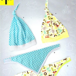 Könnte beinhalten: Ein Schnittmuster für eine Baby-Mütze und ein Lätzchen. Die Mütze ist blau mit weißen Punkten und das Lätzchen ist gelb mit einem bunten Tierdruck. Das Schnittmuster heißt "It's So Easy" und ist von Simplicity.