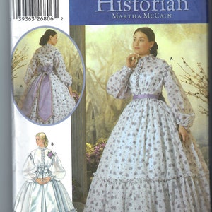 Può includere: Modello di cucito Simplicity per un abito storico. La copertina presenta una donna in un abito bianco con piccoli motivi floreali viola, maniche lunghe e scollatura a balze. Il testo "The Fashion Historian" è visibile.