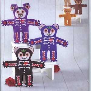 Könnte beinhalten: Ein Schnittmuster zum Nähen von vier Plüschtieren. Das Muster beinhaltet einen lila Bären, eine schwarze Katze, einen braunen Bären und eine gelbe Katze. Jedes Spielzeug hat ein Skelett-Design und ein Herz auf der Brust. Das Muster ist von Simplicity und ist für eine Größe.