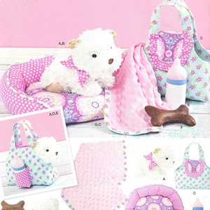 May include: Simplicity sewing pattern 1083 features a plush dog, bed, blanket, bottle, and tote bag. The dog has a pink bow and is on a pink polka dot bed. The tote bag is light blue with pink floral accents.