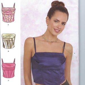 May include: Simplicity sewing pattern R12086 for a sleeveless top with a fitted bodice and a pointed hem. The pattern includes three different styles: a floral print, a satin fabric, and a solid pink fabric. The pattern is for sizes US 6-14, Euro 32-40, and French 34-42.