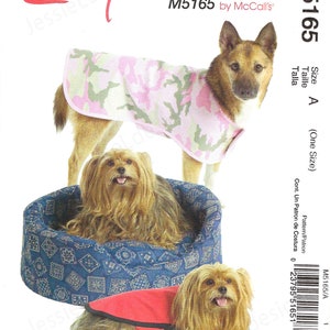 May include: A McCall's sewing pattern for dog coats and a dog bed. The pattern includes instructions for making a pink and green camouflage coat, a red coat, and a blue dog bed with a geometric pattern. The text "Easy stitch'n save" is visible.