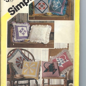 Könnte beinhalten: Simplicity Nähmuster Nummer 6146 zum Nähen von Kissen. Das Muster zeigt vier verschiedene Kissendesigns mit verschiedenen Farben und Mustern, darunter ein Blumendesign, ein Korbdesign und ein geometrisches Design. Das Muster ist für eine Größe.