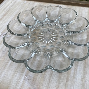 May include: Clear glass serving dish with a scalloped edge and a central starburst design. The dish is divided into sections, perfect for serving appetizers or snacks. The glass is transparent, allowing the contents to be visible.