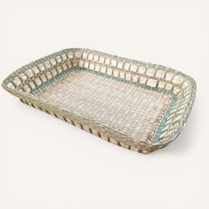 May include: Rectangular woven basket with a light green and beige color scheme. The basket has a woven base and a decorative border. The edges are reinforced with a braided design. The basket is empty and sits on a white background.