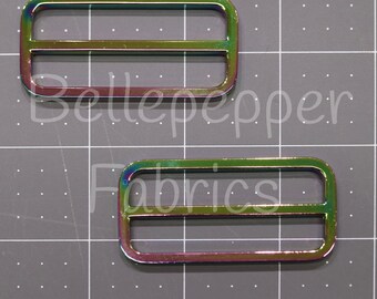 May include: Two iridescent metal slider buckles. The buckles are rectangular with rounded corners and have two horizontal bars across the center. Bellepepper Fabrics is written in white text on the image.