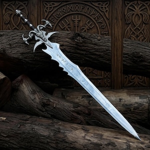 May include: A silver-toned metal sword featuring a detailed ram head guard with curved horns and a dark wrapped handle. The blade has a wavy edge design with etched runic-style characters along the center, presenting a sharp, pointed tip.