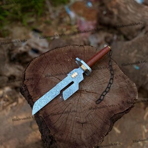 May include: A short sword with a textured silver-toned blade featuring a rectangular cutout, a brown leather-wrapped handle, a gold-toned accent piece, and a black metal chain attached to the pommel. The blade has a distinct angular design.