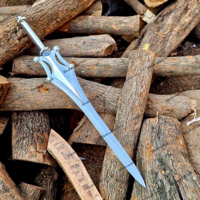 May include: A silver-colored metal sword featuring a pointed blade and a decorative crossguard with four circular accents. The handle is straight and cylindrical, leading to a pommel at the end. The blade has a central ridge and tapers to a sharp point.