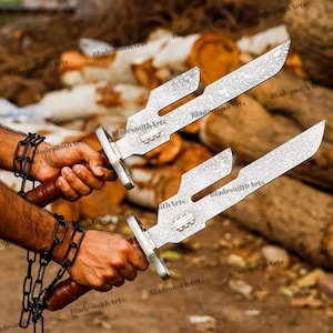May include: A pair of silver-toned metal blades with a distinct notched design and a textured finish. Each blade features a brown handle and is attached to a black metal chain. The blades have a rectangular metal guard near the handle area.