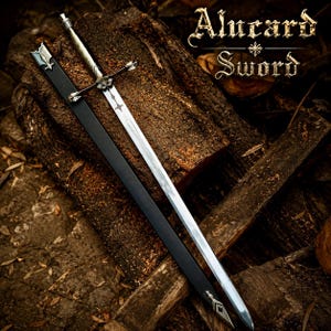Op de afbeelding: Een zilverkleurig metalen zwaard met een kruisvormige pareerstang en een zwarte schede. Het lemmet heeft een decoratieve uitsparing bij het gevest. De tekst Alucard Sword is zichtbaar in de rechterbovenhoek in een gestileerd wit lettertype.