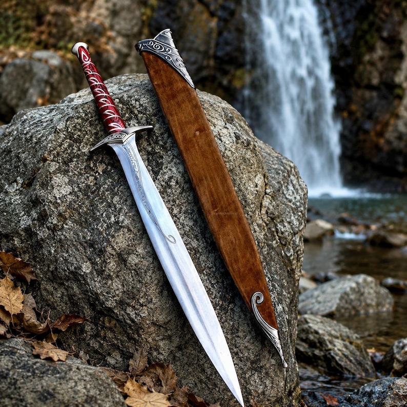May include: A silver metal sword with a red wrapped handle and intricate silver crossguard, accompanied by a brown wooden scabbard featuring silver metal accents at the top and bottom, resting against a large gray rock surface.