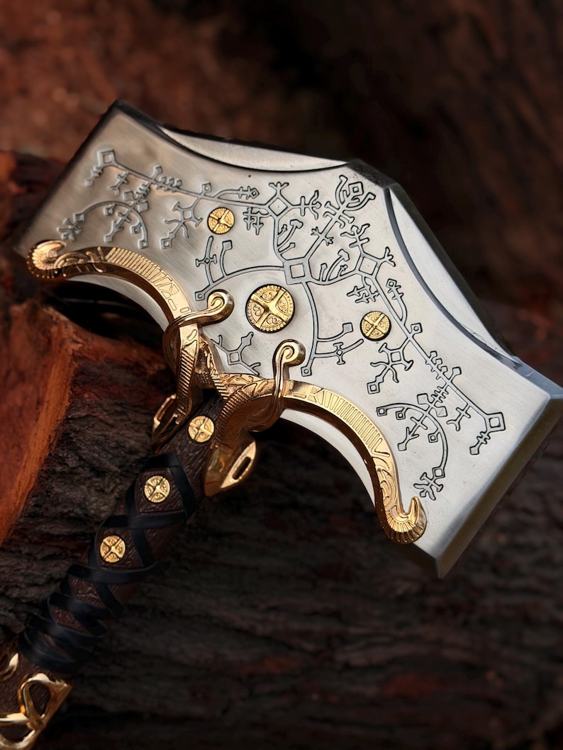 Pu&ograve; includere: Una testa d'ascia in metallo color argento con intricati motivi incisi in nero e accenti in metallo dorato. Il manico &egrave; avvolto in pelle marrone scuro con borchie circolari dorate incastonate lungo l'impugnatura e la base della testa.