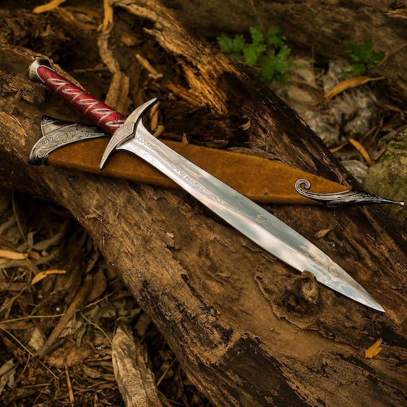 May include: A silver-toned metal sword with a pointed blade and an ornate crossguard. The handle features a deep red grip with silver filigree patterns. The sword rests partially inside a brown suede-like scabbard with silver metal accents.