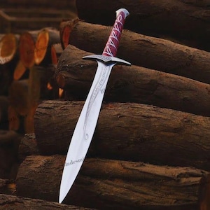 May include: A silver-toned metal sword featuring a pointed blade with intricate etched scrollwork patterns. The hilt has a metallic crossguard and a handle wrapped in a deep red material with a silver-colored pommel at the very end of the grip.