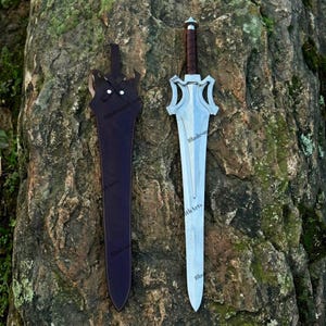 May include: A silver-toned metal sword with a pointed blade, a complex crossguard, and a brown leather-wrapped handle, accompanied by a matching dark brown leather scabbard featuring a strap and two silver-colored metal rivets at the top.