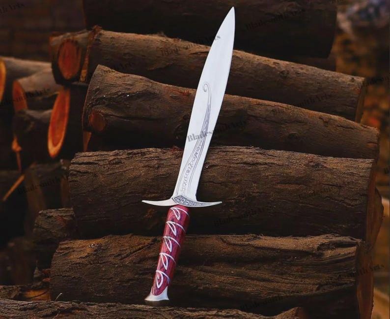 May include: A silver-colored metal dagger featuring a pointed blade with an etched swirling design and a crossguard. The handle is a deep red color with a silver-colored spiral pattern wrapping around it, ending in a flared, rounded pommel base.