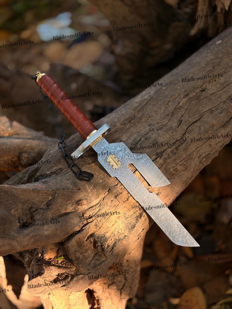 May include: A fixed-blade knife with a brown leather-wrapped handle, a gold-colored pommel and guard, and a patterned steel blade featuring a unique cutout design. A small gold-colored rectangular inlay is set into the blade near the guard.