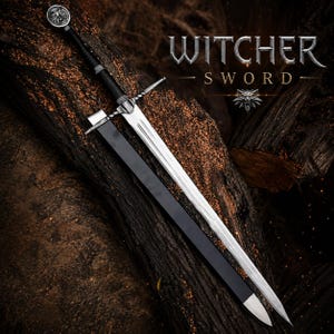 Op de afbeelding: Een zilverkleurig metalen zwaard met een zwart handvat en een wolfsembleem op de pommel, vergezeld van een zwarte schede. De tekst WITCHER SWORD en een wolfskop-icoon zijn zichtbaar in de rechterbovenhoek van de afbeelding.