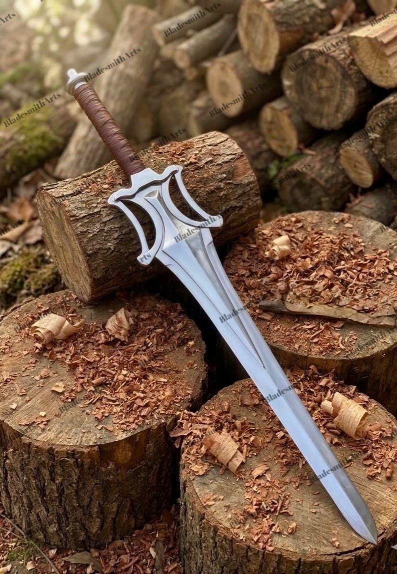 May include: A double-edged steel sword featuring a pointed blade, a central fuller, and a stylized guard with curved cutouts. The handle is wrapped in brown leather, and the pommel is a simple metal cap. The sword is positioned diagonally.