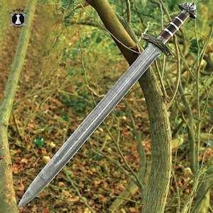 May include: A long, silver sword with a detailed hilt and a brown and white handle. The blade has a textured surface. The sword is displayed outdoors, leaning against a tree.