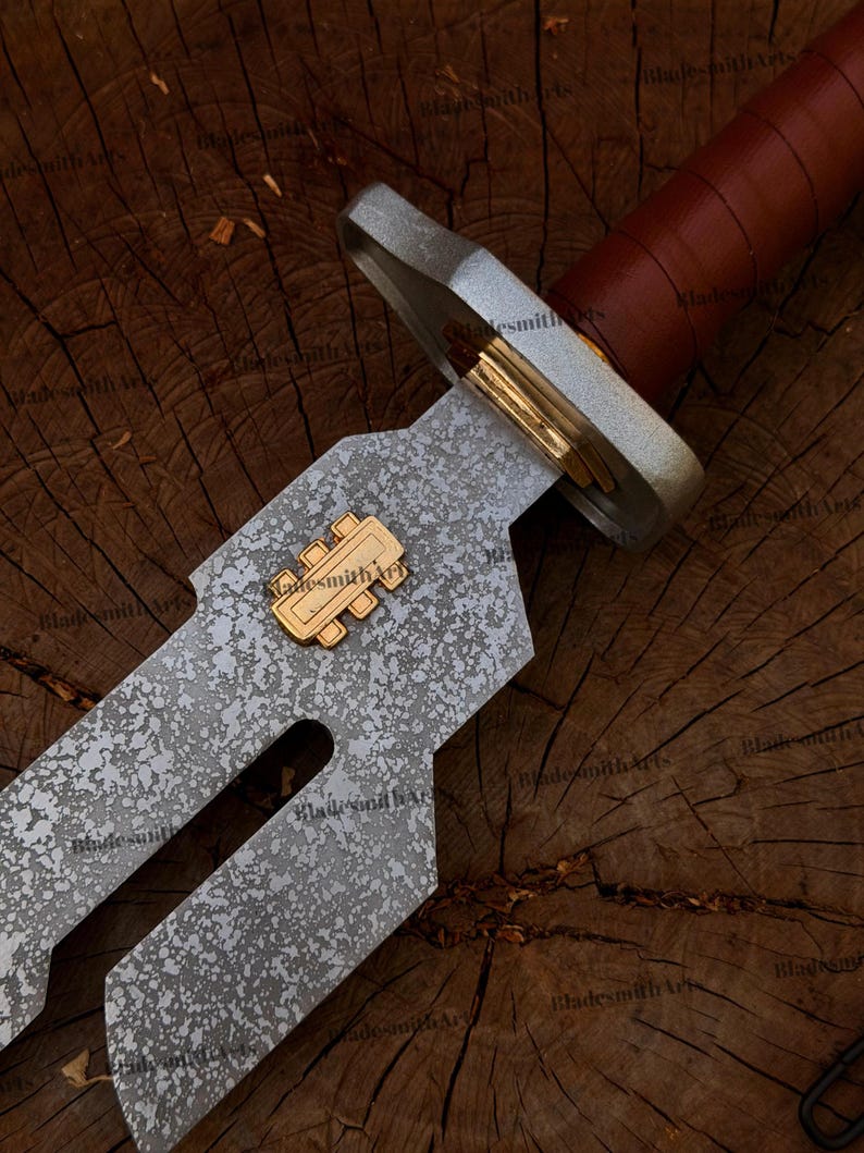 May include: A sword with a textured, mottled grey metal blade featuring a gold-colored rectangular emblem with three vertical bars. The hilt has a silver-toned crossguard, a gold-colored spacer, and a brown leather-wrapped handle.