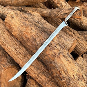 May include: A silver-toned metal sword featuring a curved blade with intricate, etched vine-like patterns running along the length of the steel. The hilt is designed with a smooth, ergonomic grip and a pommel shaped like a bird's head.