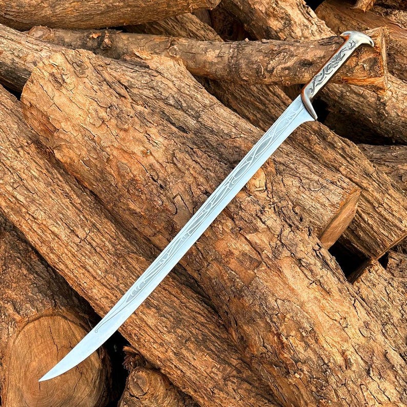 May include: A silver-toned metal sword featuring a curved blade with intricate, etched vine-like patterns running along the length of the steel. The hilt is designed with a smooth, ergonomic grip and a pommel shaped like a bird's head.