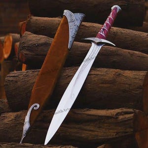 May include: A silver-toned metal sword with a pointed blade and a purple-stained wooden handle featuring white decorative accents. The sword is accompanied by a brown sheath with silver-toned metal fittings at the top and bottom ends.