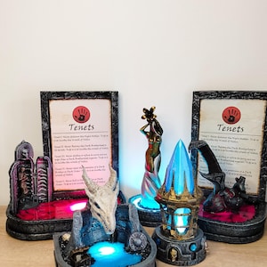 May include: A set of three fantasy themed figurines with glowing bases. The figurines are a skeletal dragon head, a female figure holding a flower, and a crystal shard. Each figurine has a small plaque with the text "Tenets" and a list of rules.