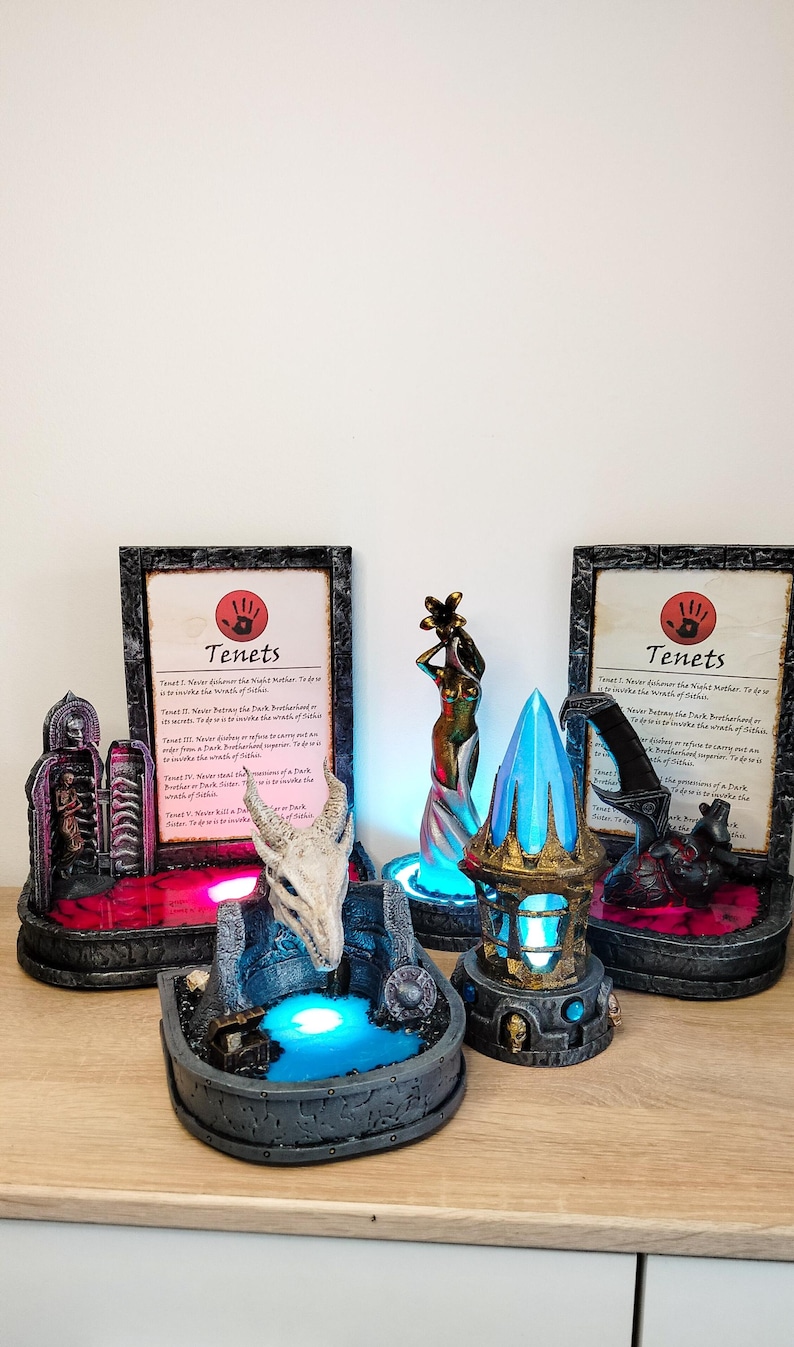 May include: A set of three fantasy themed figurines with glowing bases. The figurines are a skeletal dragon head, a female figure holding a flower, and a crystal shard. Each figurine has a small plaque with the text "Tenets" and a list of rules.