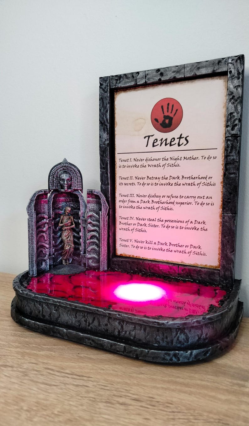 May include: A dark grey stone fountain with a red liquid inside. The fountain has a small statue of a woman inside. A framed piece of paper with the text "Tenets" and a list of rules is behind the fountain.