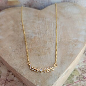 May include: A gold chain necklace with a delicate leaf design and a small clear crystal in the center.