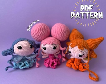 May include: Three crocheted dolls with large heads and small bodies. The left doll is blue, the center doll is pink with two large buns, and the right doll is orange with glasses. Text reads PDF PATTERN and @latersart. The dolls have black eyes.