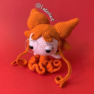 May include: A crochet doll with bright orange hair styled in two large pointed buns and long curled strands. The doll has a pale pink face, black bead eyes, and thin gold-toned wire glasses. The text @latersart is visible above the doll.