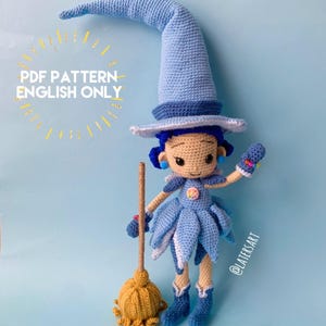 May include: A crocheted doll wearing a tall light blue pointed hat, a blue dress with petal-like layers, and blue boots. The doll has dark blue hair, holds a tan broom with a yellow base, and features the text PDF PATTERN ENGLISH ONLY.